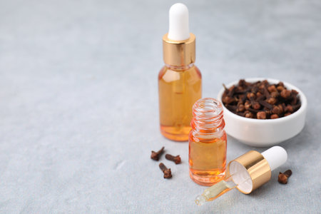Clove oil in bottles, pipette and dried buds on gray table, closeup. Space for textの写真素材