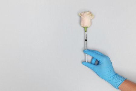 Doctor making injection to rose on light gray background, top view. Space for text