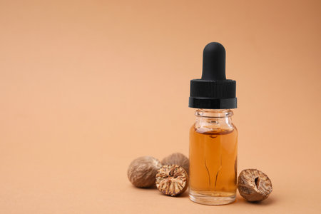 Nutmeg essential oil and nuts on beige background, closeup. Space for textの写真素材