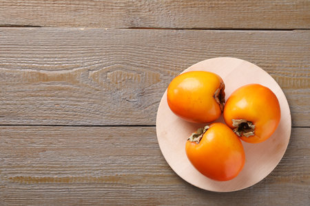 Delicious ripe persimmons on wooden table, top view. Space for textの写真素材