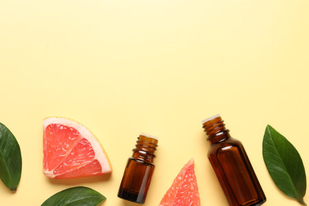Grapefruit essential oil in bottles, leaves and cut fruit on yellow table, flat lay. Space for textの写真素材