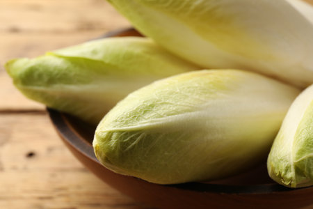 Fresh raw Belgian endives (chicory) in bowl on wooden table, closeup