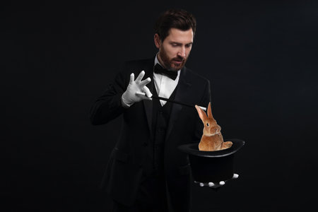 Magician showing trick with top hat and rabbit on black backgroundの写真素材