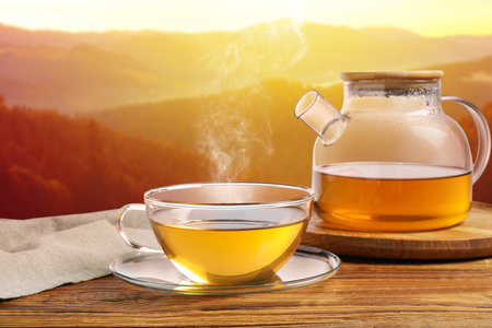 Aromatic green tea in glass cup and teapot on wooden table in mountainsの写真素材