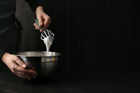 Woman making whipped cream with whiskey at black table, closeup. Space for text