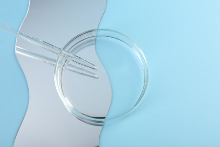 Empty petri dish, pipette and mirror on light blue background, flat lay. Space for textの写真素材
