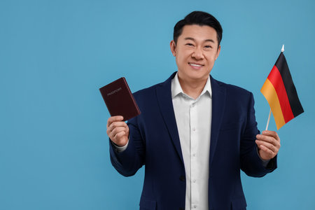 Immigration. Happy man with passport and flag of Germany on light blue background, space for textの写真素材