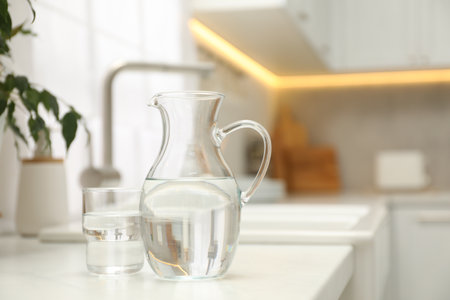 Jug and glass with clear water on white table in kitchen, space for textの写真素材