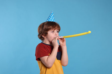 Birthday celebration. Cute little boy in party hat with blower on light blue backgroundの写真素材