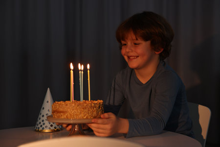 Cute boy with birthday cake at table indoorsの写真素材