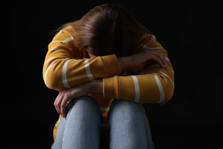 Sadness. Upset woman sitting on black backgroundの写真素材