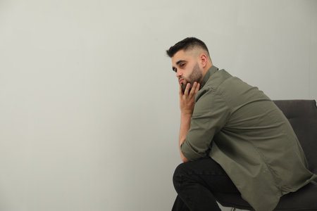 Sad man sitting near light gray wall. Space for textの写真素材