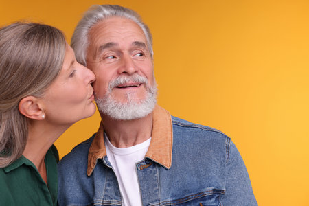 Senior woman kissing her beloved man on orange background, space for textの写真素材