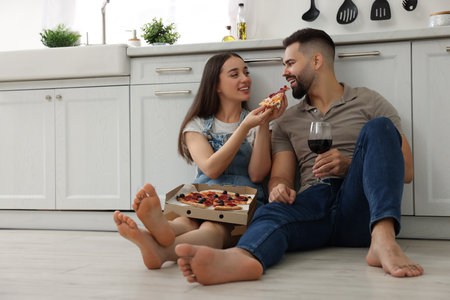 Happy young couple eating pizza in kitchen. Space for textの写真素材