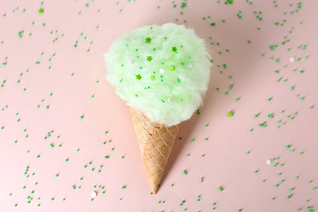 Sweet cotton candy in waffle cone on beige background, top view