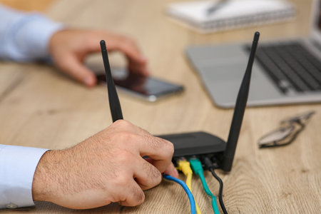 Man inserting cable into Wi-Fi router at wooden table indoors, closeupの写真素材