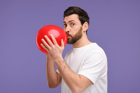 Man inflating red balloon on purple background