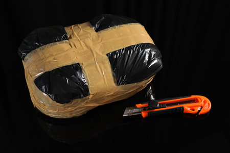 Smuggling, drug trafficking. Package with narcotics and utility knife on black surface