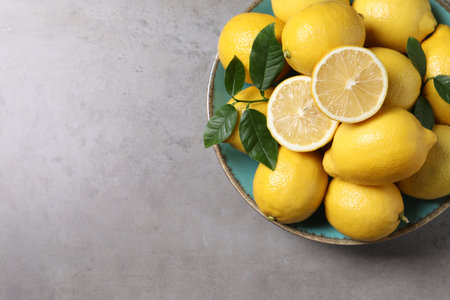 Fresh lemons and green leaves on gray table, top view. Space for textの写真素材
