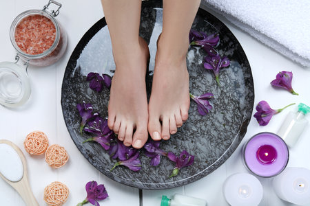 Woman soaking her feet in bowl with water and flowers on white wooden floor, top view. Spa treatmentの写真素材