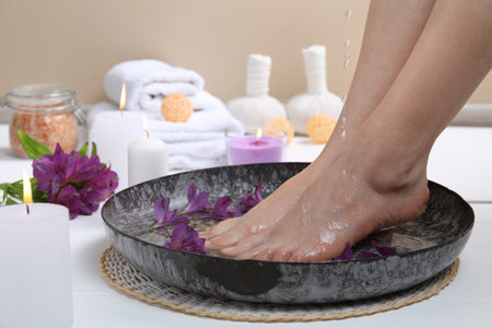 Woman pouring water onto her feet in bowl on white floor, closeup. Spa treatmentの写真素材