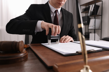 Notary stamping document at wooden table in office, closeup