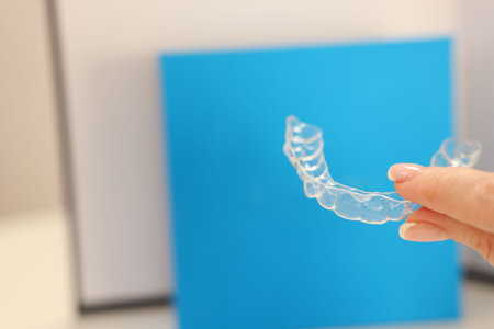 Woman with transparent dental aligner on blurred background, closeup. Space for textの写真素材