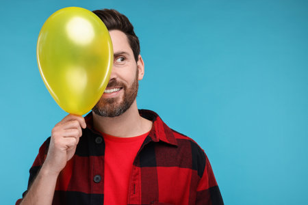 Happy man with yellow balloon on light blue background. Space for textの写真素材