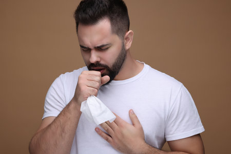 Sick man with tissue coughing on brown backgroundの写真素材