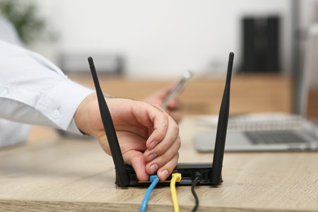 Man inserting cable into Wi-Fi router at wooden table indoors, closeupの写真素材
