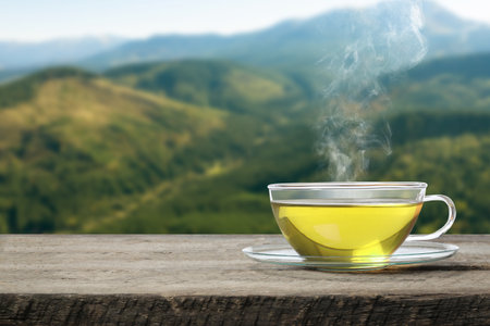 Aromatic green tea in glass cup on wooden table in mountains, space for textの写真素材