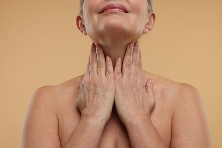 Mature woman touching her neck on beige background, closeupの写真素材