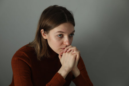 Sad young woman near gray wall indoors, space for text