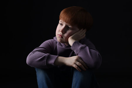 Portrait of sad little boy on black background