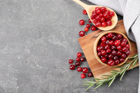 Fresh ripe cranberries and rosemary on gray table, flat lay. Space for text