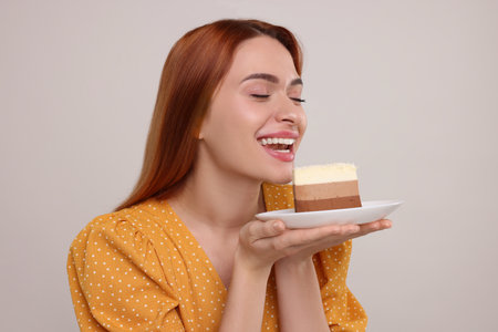 Young woman with piece of tasty cake on light gray backgroundの写真素材