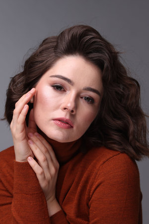 Portrait of beautiful young woman with wavy hairstyle on gray background