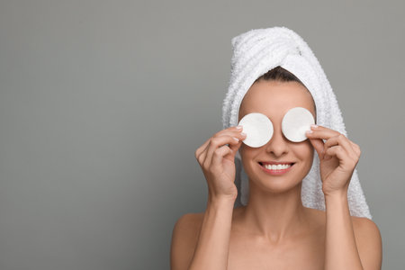 Smiling woman removing makeup with cotton pads on gray background. Space for textの写真素材