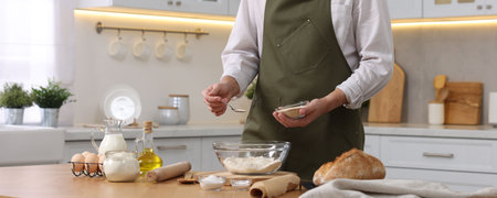 Making bread. Man putting dry yeast into bowl with flour at wooden table in kitchen, closeup