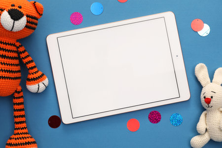 Modern tablet, confetti and stuffed animals on blue background, flat lay. Space for textの写真素材