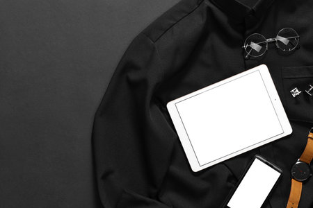 Modern tablet, smartphone, watch, shirt and glasses on black background, top view. Space for textの写真素材