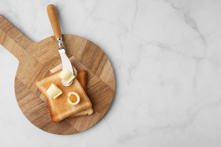 Tasty butter curls, knife and toasts on white marble table, top view. Space for textの写真素材