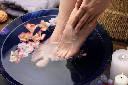 Woman soaking her feet in bowl with water and flowers on floor, closeup. Spa treatmentの写真素材