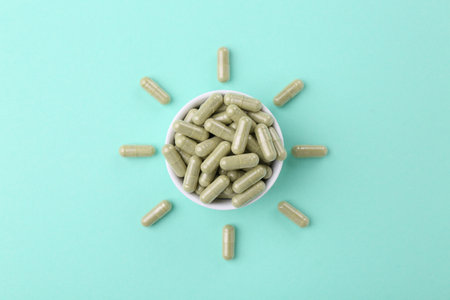 Bowl with vitamin capsules on turquoise background, top viewの写真素材