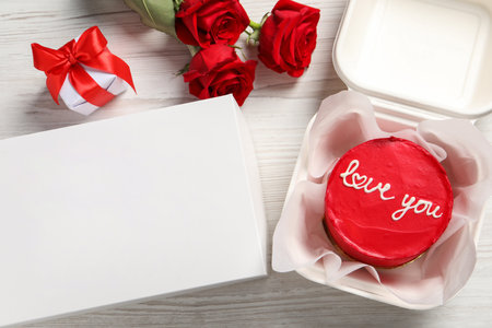 Tasty bento cake in takeaway packaging, roses and gift box on white wooden table, flat layの写真素材