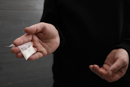 Drug addiction. Man with plastic bag of cocaine on gray background, closeup