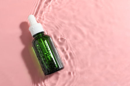 Bottle of cosmetic product in water on pink background, top view. Space for textの写真素材
