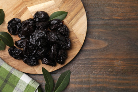 Tasty dried prunes and green leaves on wooden table, top view. Space for textの写真素材