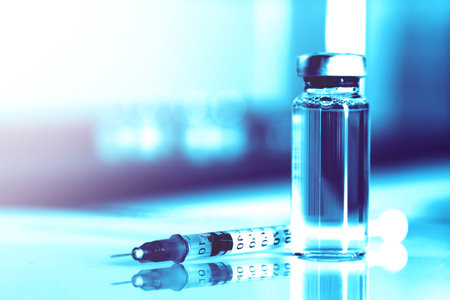 Syringe and glass vial with medication on mirror surface, toned in light blueの写真素材