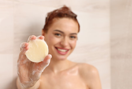 Happy young woman with solid shampoo bar in shower, selective focus. Space for textの写真素材